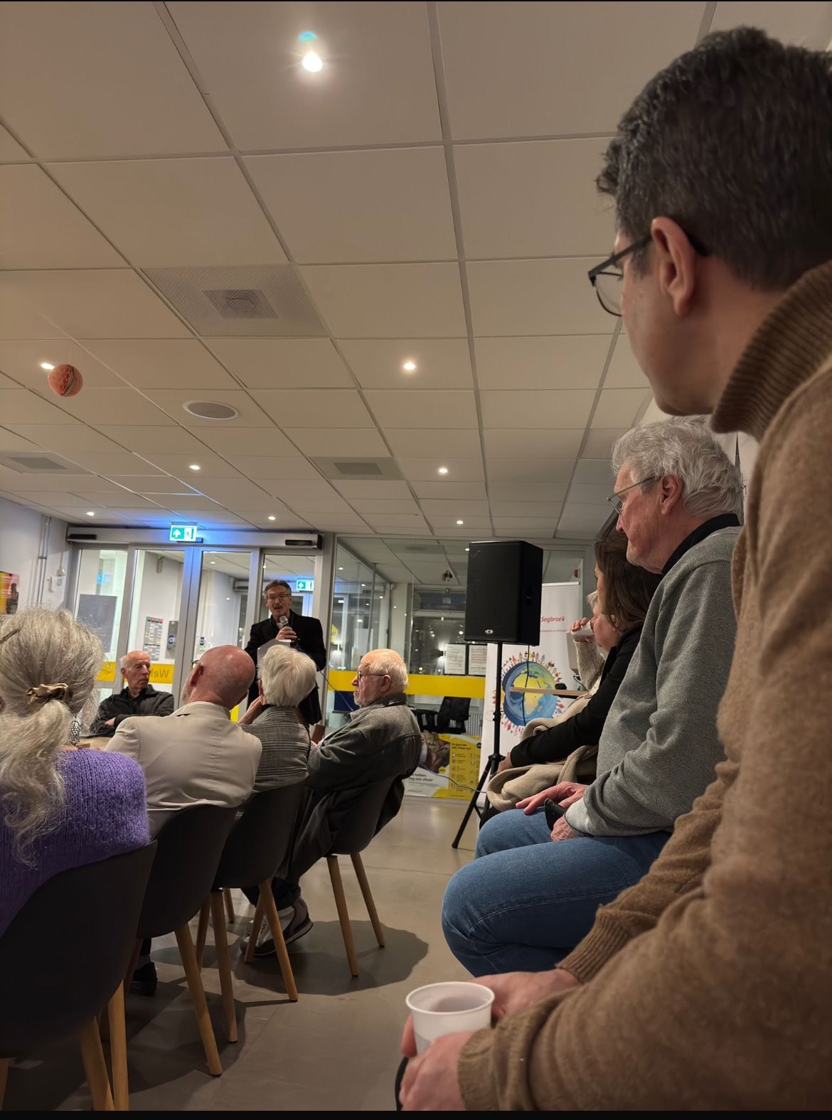 Gasten luisteren naar een spreker tijdens de nieuwjaarsreceptie van Stichting Kleurrijk Segbroek