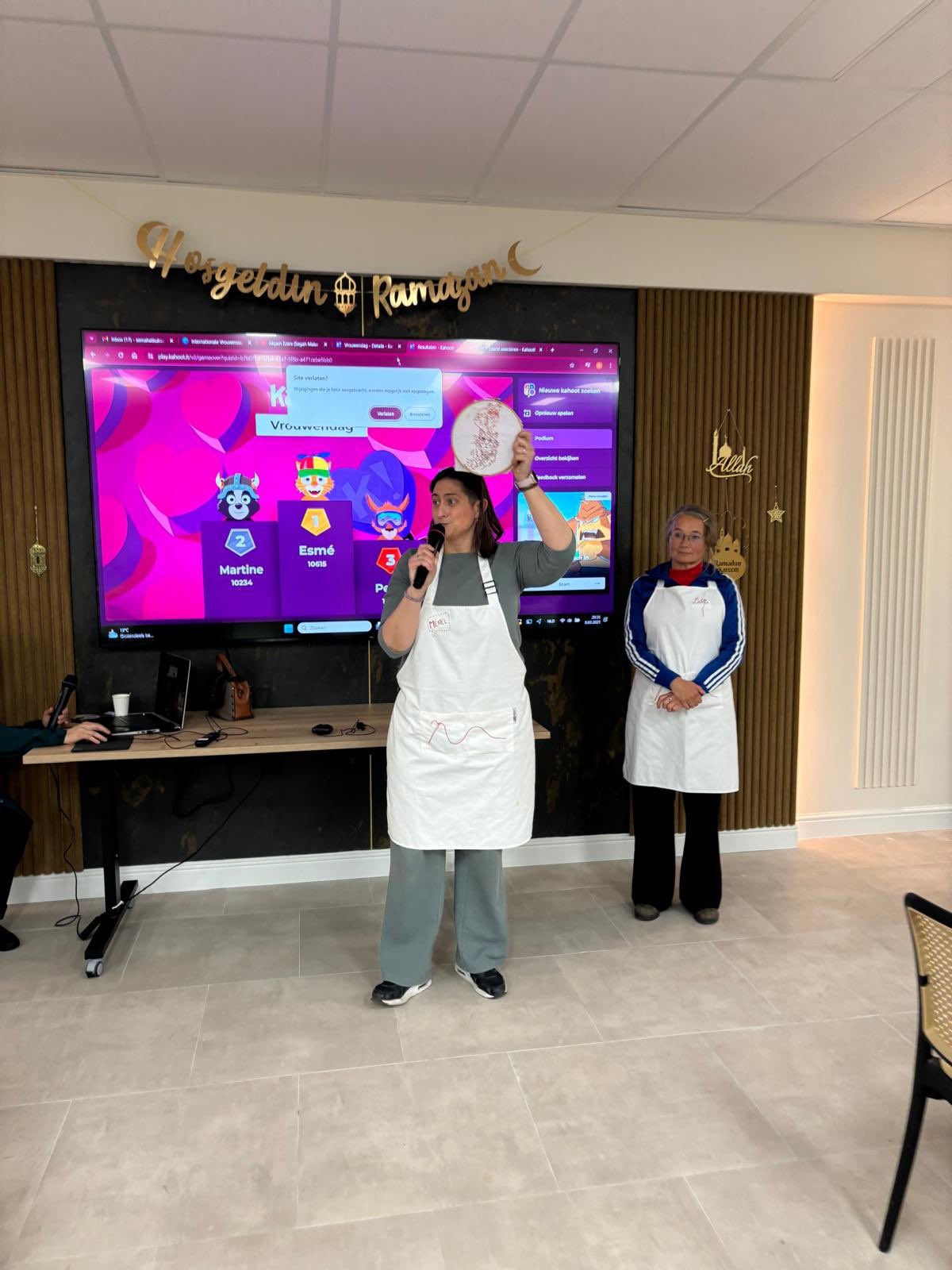 Twee vrouwen presenteren de quiz voor een groot scherm tijdens de vrouwendagviering