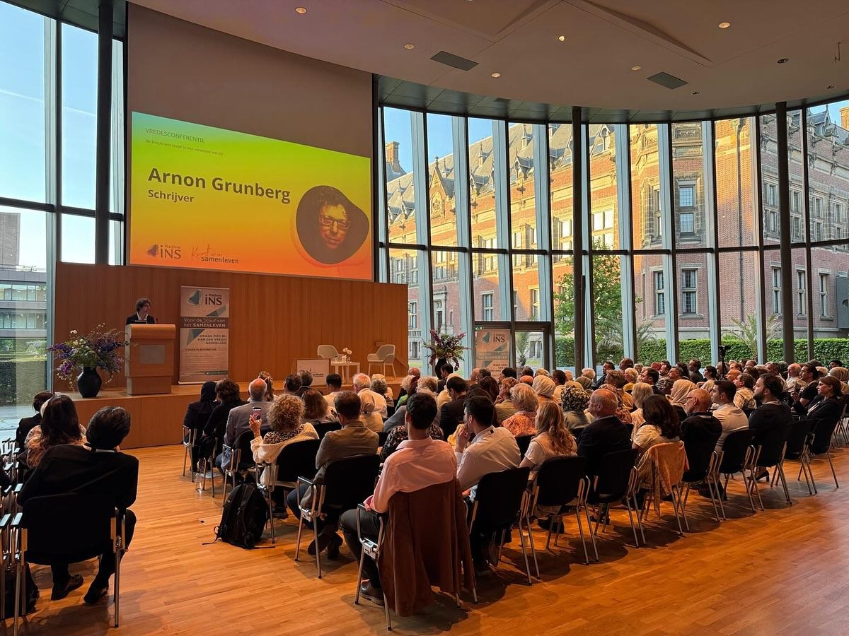 Een volle zaal in het Vredespaleis tijdens de conferentie, met Arnon Grunberg op het scherm